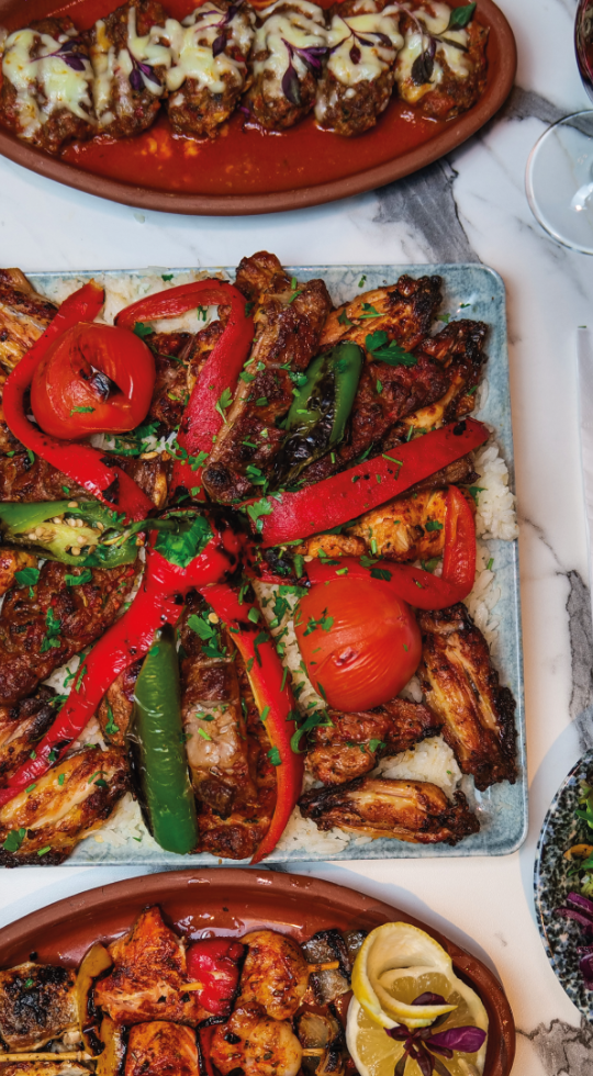 Close up of hummus drizzled with oil and adana kebabs on flatbreads